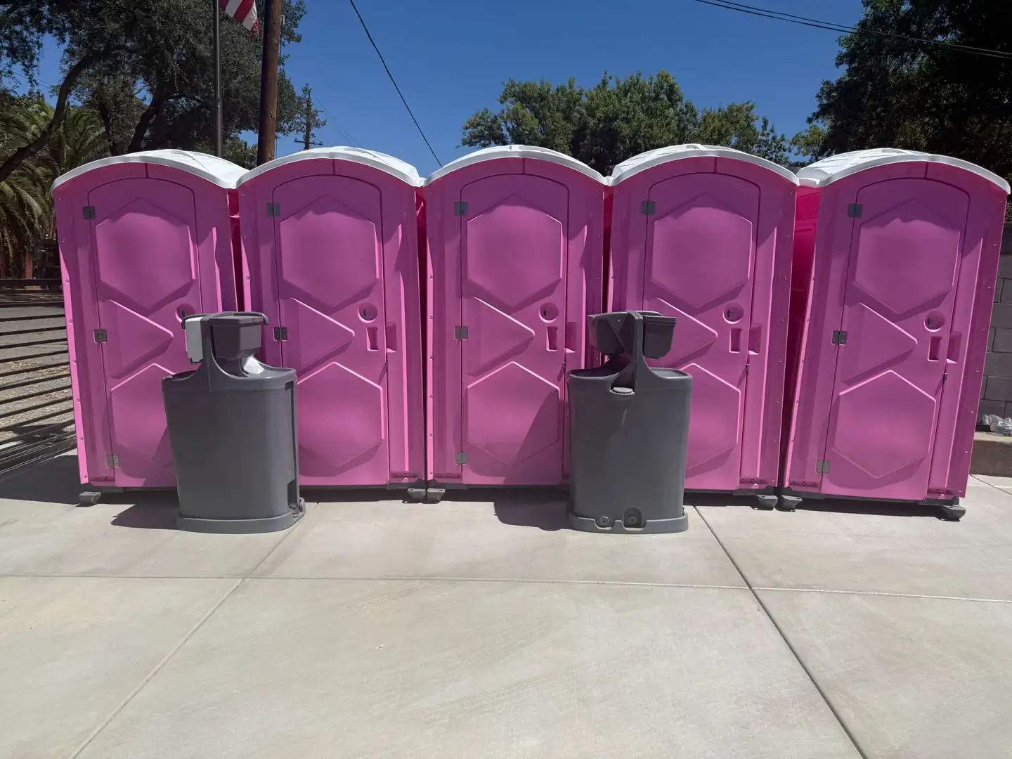 Pink and blue portable toilets lined up with two freestanding handwashing stations