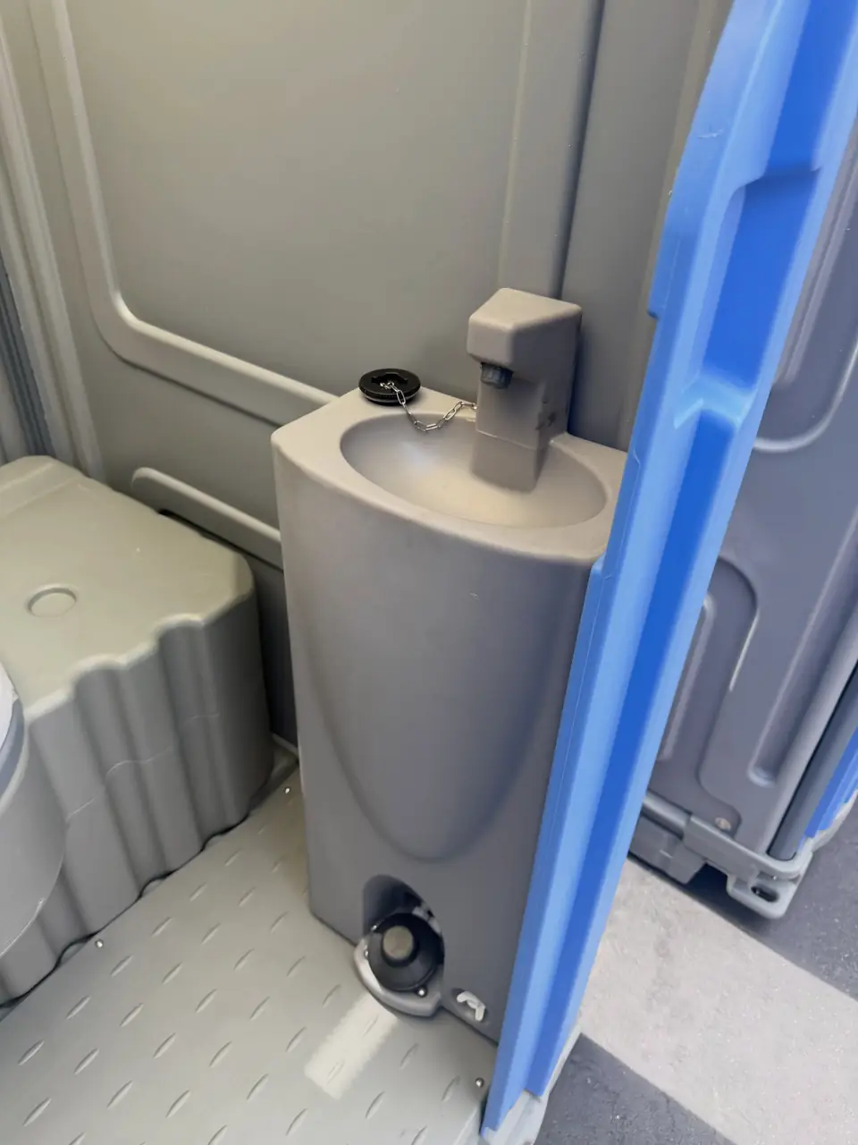 Gray molded sink with a foot pump inside a deluxe portable toilet
