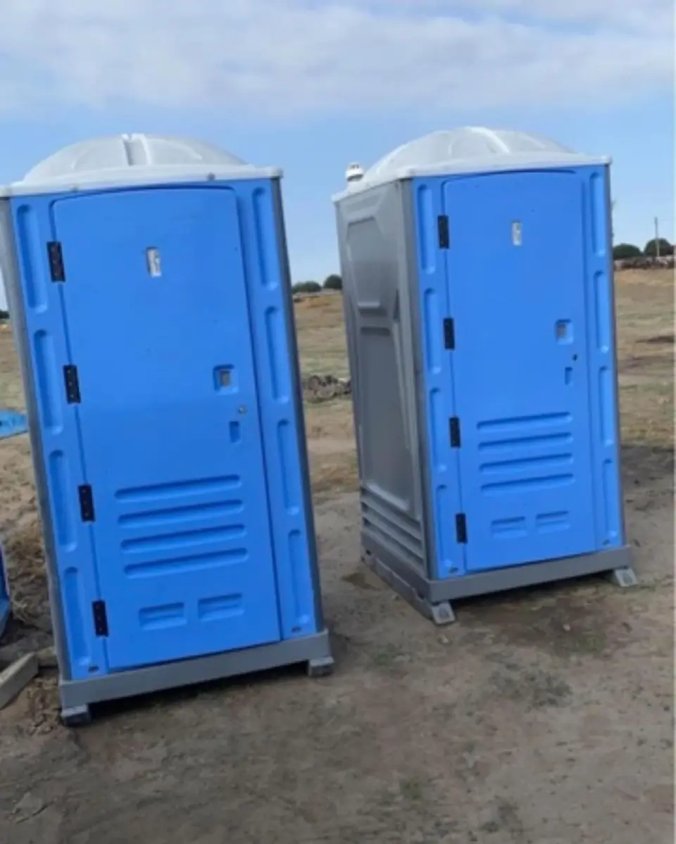 Two blue standard portable toilets standing on open ground